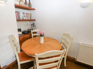 A corner dining area with a round wooden table and four chairs with a vase of flowers on the table and shelves with books at Inglenook Cottage in Broad Haven