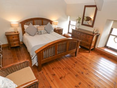 A bedroom with a wooden bed frame two nightstands a wooden dresser with a mirror and hardwood floor at Inglenook Cottage in Broad Haven