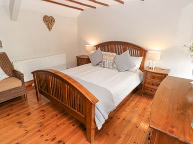 A bedroom with a wooden bed frame two bedside tables with lamps a wicker chair and wooden floor at Inglenook Cottage in Broad Haven
