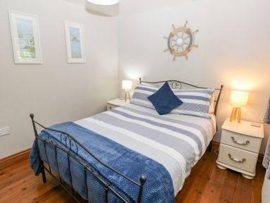 A bedroom with a metal frame bed striped bedding blue throw pillows and two bedside tables with lamps at Inglenook Cottage in Broad Haven