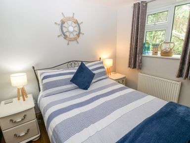 A bedroom with a bed striped bedding two bedside tables with lamps a window with curtains and nautical decor at Inglenook Cottage in Broad Haven