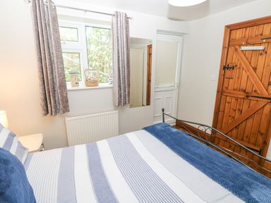 A bedroom with a striped bedspread a wooden door a window with curtains and a radiator at Inglenook Cottage in Broad Haven