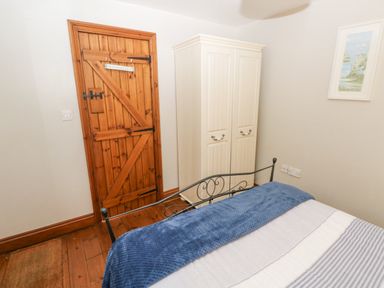 A bedroom with a wooden door a white wardrobe a bed with blue and white bedding and a framed picture on the wall at Inglenook Cottage in Broad Haven