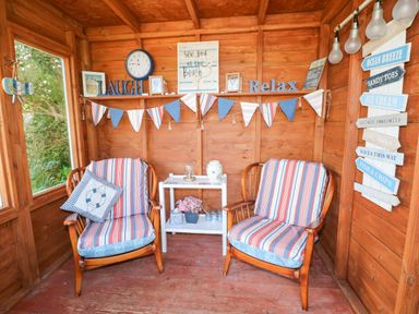 A wooden room with two striped cushioned chairs a small white side table with decorations and beach themed wall signs at Inglenook Cottage in Broad Haven