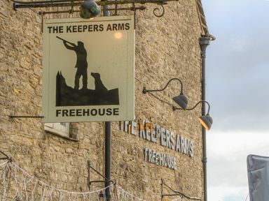 A stone building with a sign reading The Keepers Arms Freehouse and an illustration of a person with dogs at 3 Painters Field Quenington Near Cirencester