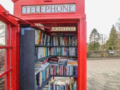 Inside a red telephone box repurposed as a small library with shelves filled with books at 3 Painters Field Quenington Near Cirencester