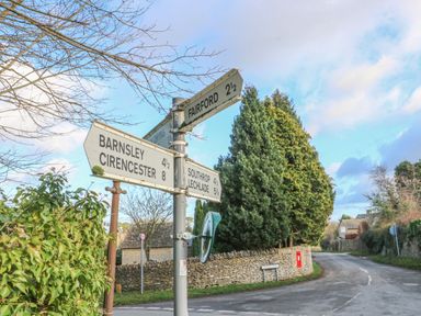 A rural road junction with directional signs pointing to Fairford Barnsley Cirencester Southrop and Lechlade with trees and stone walls in the background at 3 Painters Field Quenington Near Cirencester