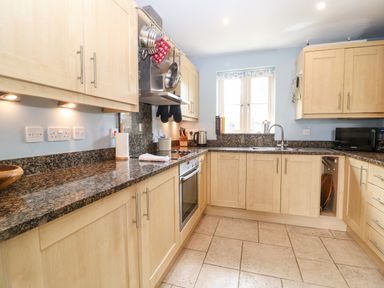 A kitchen with wooden cabinets granite countertops a stove microwave sink and window at 3 Painters Field Quenington Near Cirencester