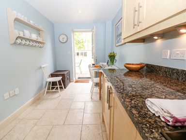 A kitchen with blue walls white chairs granite countertop and a door leading outside at 3 Painters Field Quenington Near Cirencester
