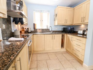 A kitchen with wooden cabinets a stove oven a microwave toaster and a window at 3 Painters Field Quenington Near Cirencester