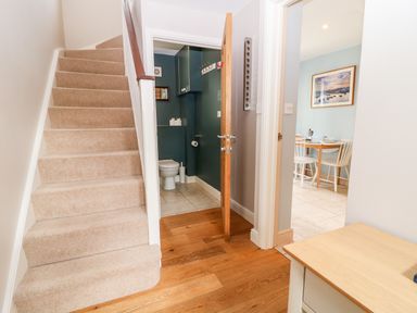 A hallway with carpeted stairs wooden flooring a small bathroom with a toilet and a dining area with a table and chairs at 3 Painters Field Quenington Near Cirencester