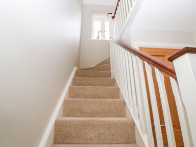 A carpeted staircase with white railings and wooden handrails leading up to a window and a wooden door 3 Painters Field Quenington Near Cirencester
