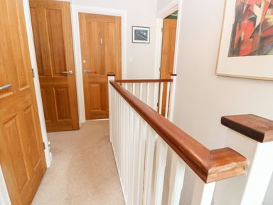 A hallway with wooden doors a handrail and framed artwork at 3 Painters Field in Quenington Near Cirencester