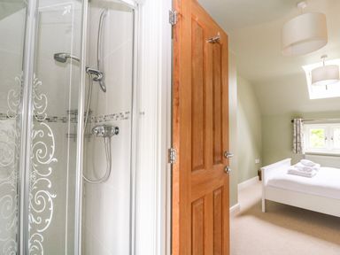 A bathroom with a glass shower enclosure next to a bedroom with a bed and folded towels at 3 Painters Field Quenington Near Cirencester