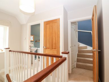 A hallway with wooden doors a staircase and a bathroom at 3 Painters Field in Quenington Near Cirencester