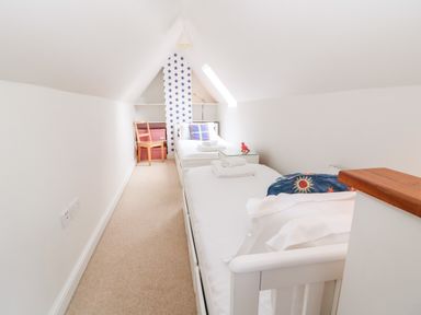 A narrow attic bedroom with two single beds and a chair at 3 Painters Field in Quenington Near Cirencester