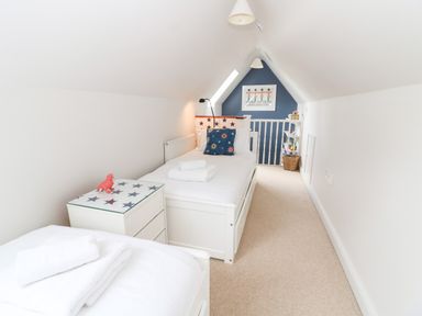 A narrow attic bedroom with two single beds towels on beds and star decorated furniture at 3 Painters Field in Quenington Near Cirencester