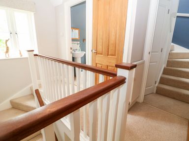 A staircase landing with beige carpet wooden doors and a white railing at 3 Painters Field Quenington Near Cirencester