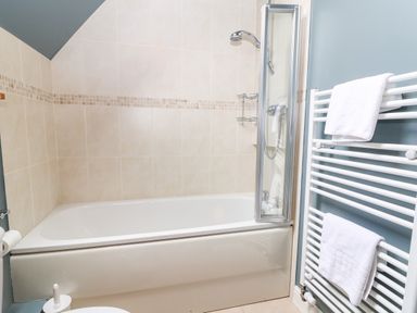 A bathroom with a bathtub shower unit and a white towel radiator at 3 Painters Field Quenington Near Cirencester