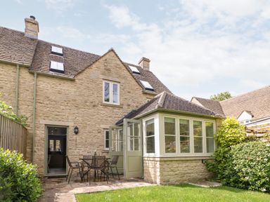 A stone house with a patio table and chairs outside and a small garden at 3 Painters Field Quenington Near Cirencester