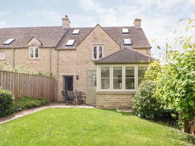 A stone house with a green lawn patio table and chairs in the garden at 3 Painters Field in Quenington Near Cirencester