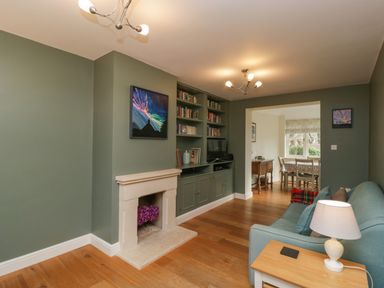 A living room with built in bookshelves and a fireplace leading to a dining area at 3 Painters Field Quenington Near Cirencester