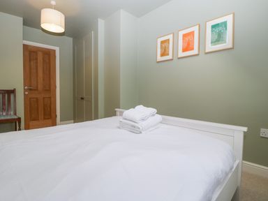 A bedroom with a white bed and folded towels on it three framed pictures on wall and a wooden door at 3 Painters Field in Quenington Near Cirencester