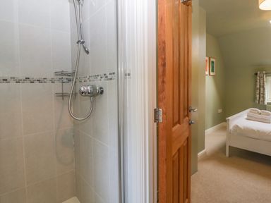 A bathroom shower next to an open wooden door leading to a bedroom with a bed and folded towels at 3 Painters Field in Quenington near Cirencester