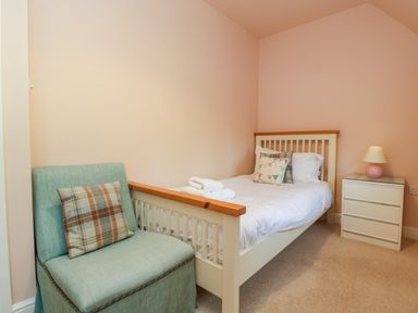 A bedroom with a single bed a side table with a lamp and a chair with a cushion at 3 Painters Field in Quenington Near Cirencester