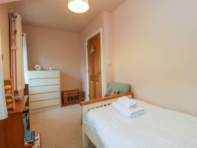 A bedroom with a single bed with folded towels a chest of drawers a wooden door and a small armchair at 3 Painters Field Quenington Near Cirencester