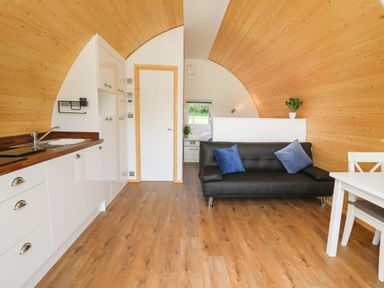 An open plan room with a kitchen area on the left a black sofa with blue cushions and a white dining table with chairs at Seren in Llandrindod Wells
