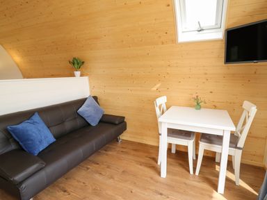 A small room with a brown sofa blue cushions a white table with two chairs and a wall-mounted television at Seren in Llandrindod Wells