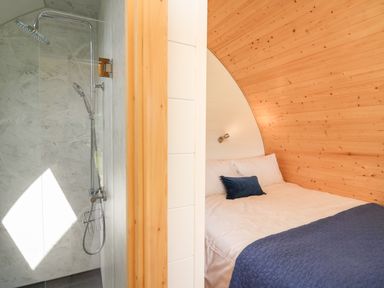 A bedroom with a blue blanket and a pillow next to a bathroom with a shower at Seren in Llandrindod Wells