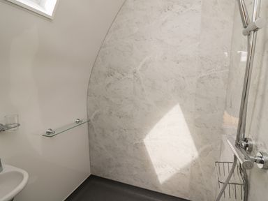 A bathroom shower area with a handheld showerhead a glass shelf and a small washbasin at Seren in Llandrindod Wells