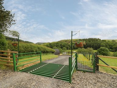 A driveway gate with hanging flower baskets and a cattle grid on a rural road at Seren in Llandrindod Wells