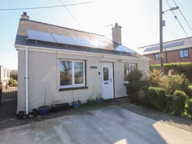 A small house with solar panels on the roof and potted plants by the door at Tanyfron Holiday Studio in Bryngwran near Gwalchmai