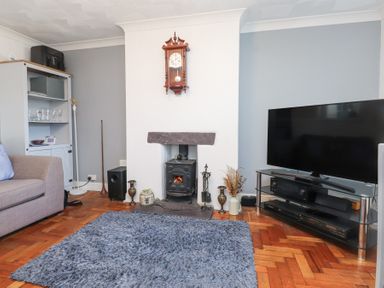 A living room with a fireplace clock television cabinet and gray rug at Tanyfron Holiday Studio Bryngwran near Gwalchmai