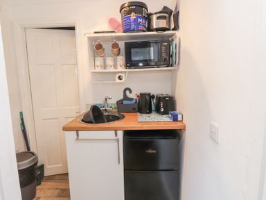 A small kitchen area with a sink, microwave on a shelf, kettle, toaster, and a mini fridge at Tanyfron Holiday Studio in Bryngwran near Gwalchmai