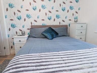 A bedroom with a bed flanked by two white nightstands and floral wallpaper at Tanyfron Holiday Studio in Bryngwran near Gwalchmai