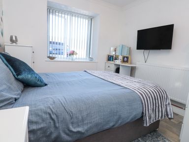 A bedroom with a bed a window with vertical blinds a television on the wall and a dressing table at Tanyfron Holiday Studio Bryngwran near Gwalchmai