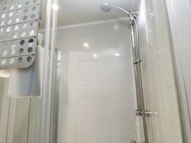 A bathroom shower area with a handheld showerhead and a hanging grey shower caddy at Tanyfron Holiday Studio Bryngwran near Gwalchmai