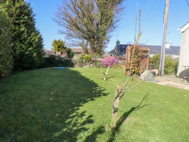 A garden with grass trees and shrubs near houses at Tanyfron Holiday Studio in Bryngwran near Gwalchmai