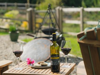 A wooden table with a bottle of red wine two glasses with red wine and a plate with food outdoors at Onnen in Oakford near Aberaeron