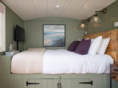 A bedroom with a bed featuring white and purple pillows wall lamps a painting and a television at Onnen in Oakford near Aberaeron