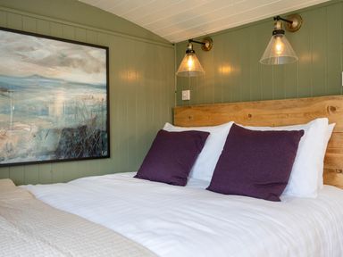 A bedroom with a wooden headboard a bed with white linens and purple pillows two wall lamps and a large painting on green walls at Onnen Oakford near Aberaeron