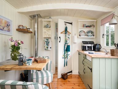 A small kitchen area with striped chairs wooden table shelves with dishes and aprons at Onnen in Oakford near Aberaeron