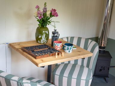 A wooden table with a chess set flowers in a vase two mugs and a striped chair at Onnen in Oakford near Aberaeron