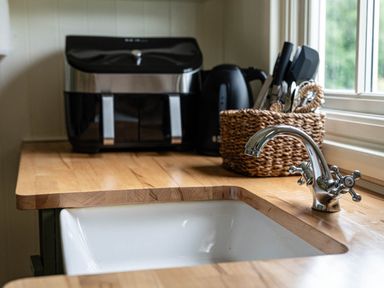 A kitchen sink with a faucet on a wooden countertop with an air fryer kettle and utensils in a basket beside a window at Onnen in Oakford near Aberaeron
