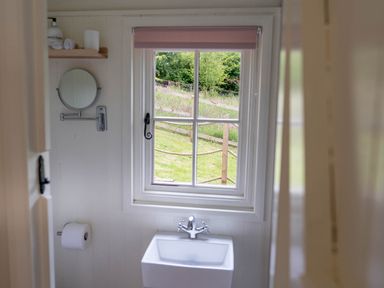 A bathroom window with a small sink below and a round mirror on the wall at Onnen in Oakford near Aberaeron