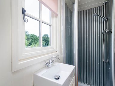 A bathroom with a white sink under a window and a shower with corrugated metal walls at Onnen in Oakford near Aberaeron